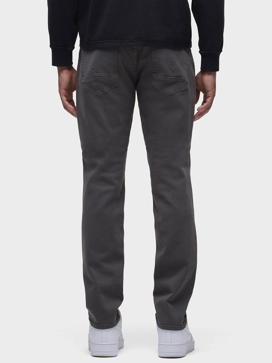 Back view of a person in Hudson Blake Slim Straight Twill Pant in Grey and a black shirt, with white sneakers peeking out.