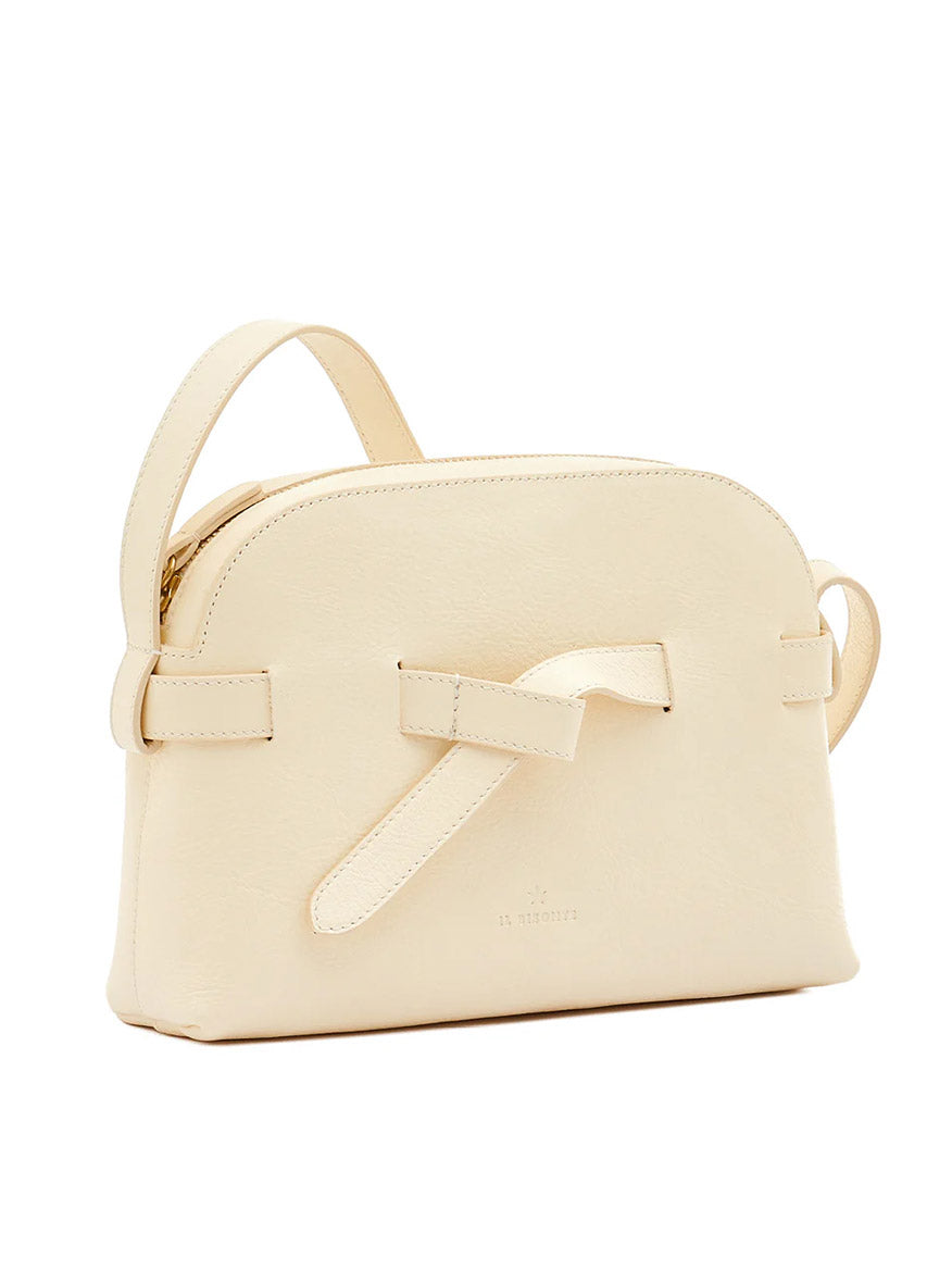 The Il Bisonte Elisa Crossbody in white cowhide leather features a minimalist design, top handle, and a decorative bow on the front.