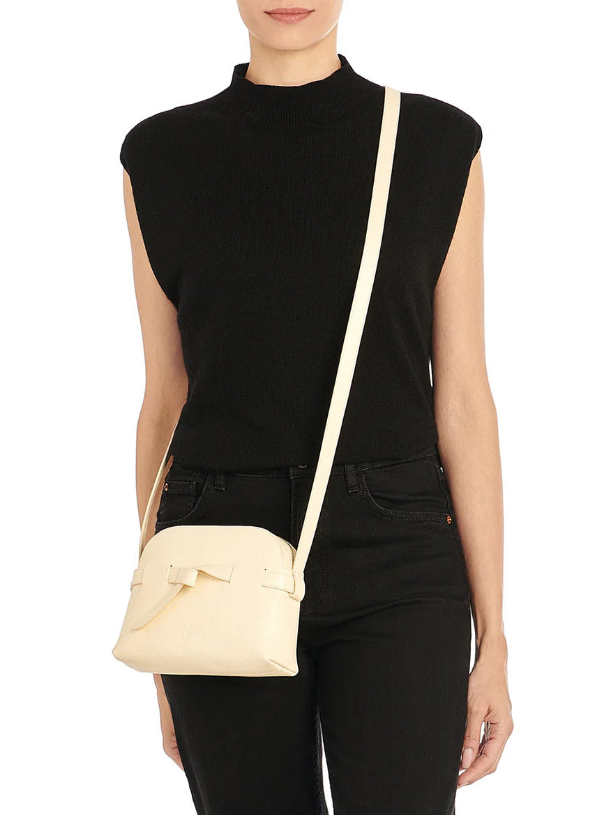 A woman in a sleeveless black top and black pants carries the Il Bisonte Elisa Crossbody in white cowhide leather, made in Italy, over her shoulder.