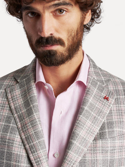 A man with curly hair wearing an unbuttoned pink Isaia Capri Sport Jacket in Rustic Grey with Cream/Pink Plaid under a patterned grey blazer inspired by Capri, Italy.