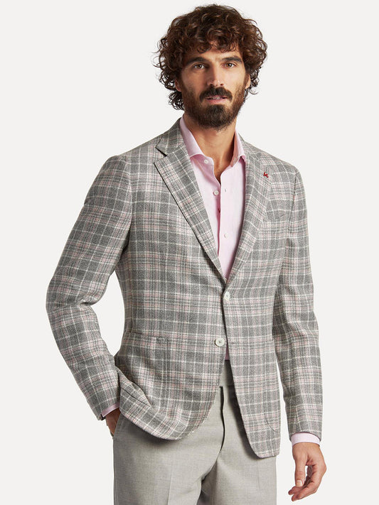 A man with curly hair wearing an Isaia Capri Sport Jacket in Rustic Grey with Cream/Pink Plaid, a pink shirt, and light gray trousers.