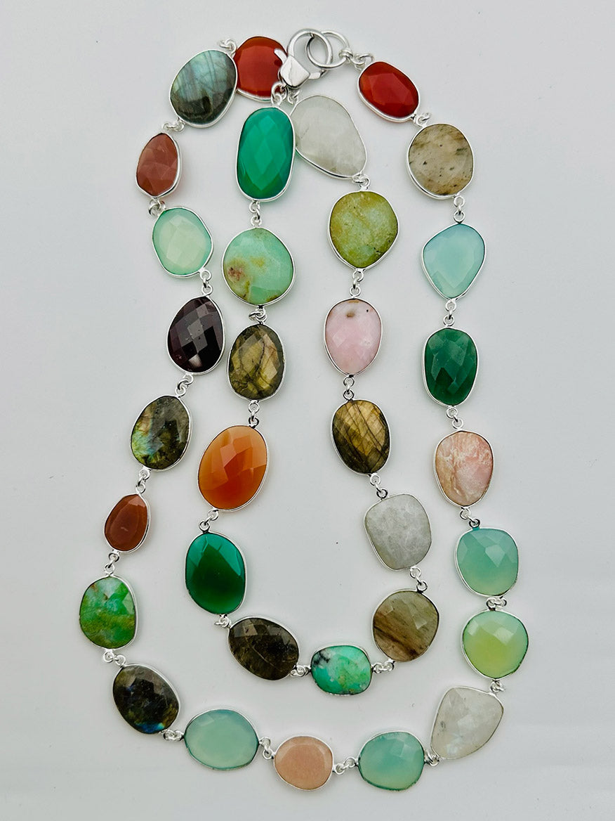 Introducing the JMNYC Designs 36" Multi Gemstone Sterling Silver Necklace, a striking accessory showcasing irregular, multicolored gemstone beads set in sterling silver and artfully arranged in two overlapping strands against a white background.