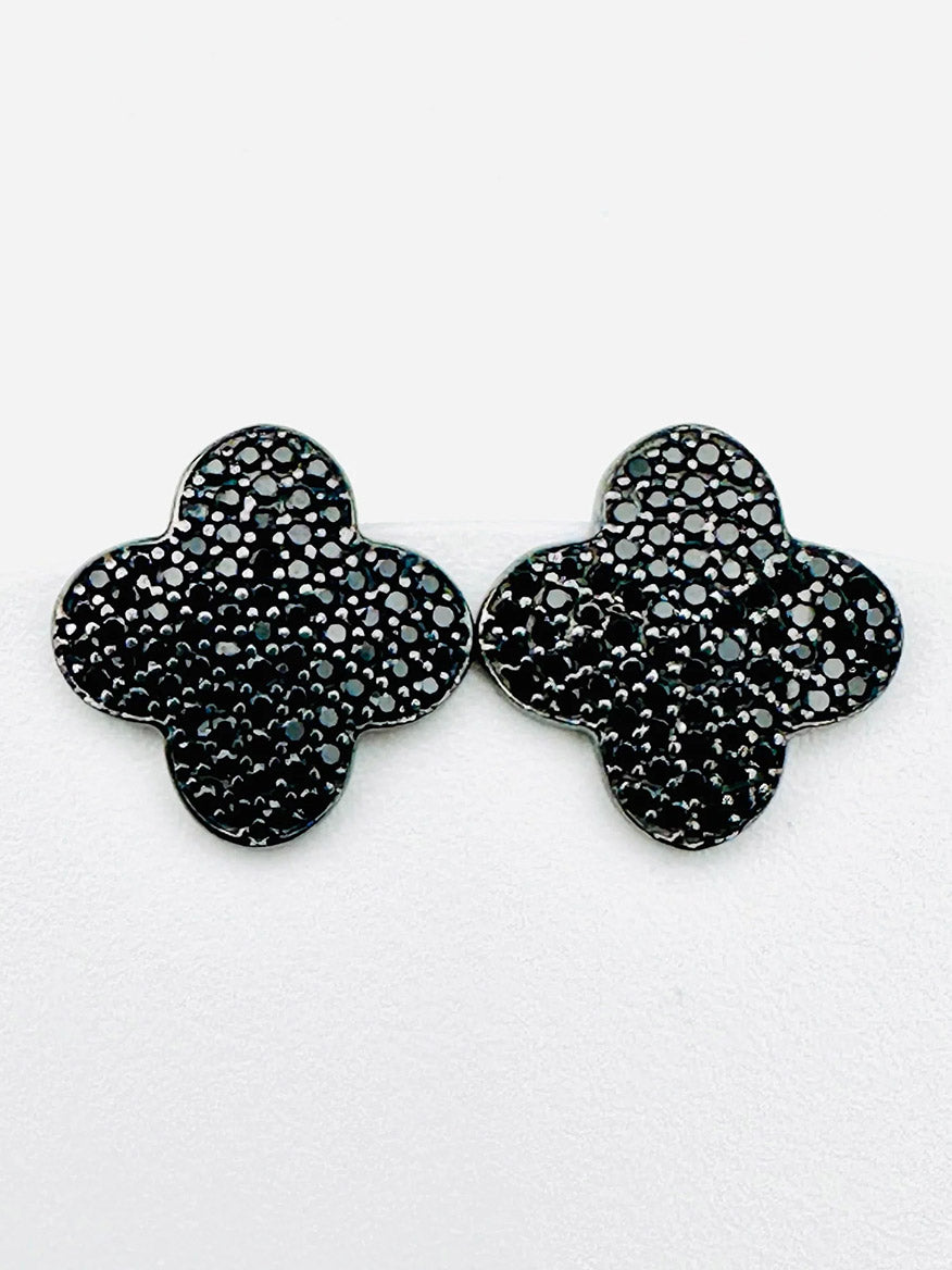 Introducing the JMNYC Designs Black Spinel Sterling Silver Clover Shaped Stud, 1.25"—a pair of striking black, four-leaf clover-shaped stud earrings carefully crafted in sterling silver. These earrings feature a textured, beaded surface accented with subtle Black Spinel stones and are beautifully displayed against a white background.