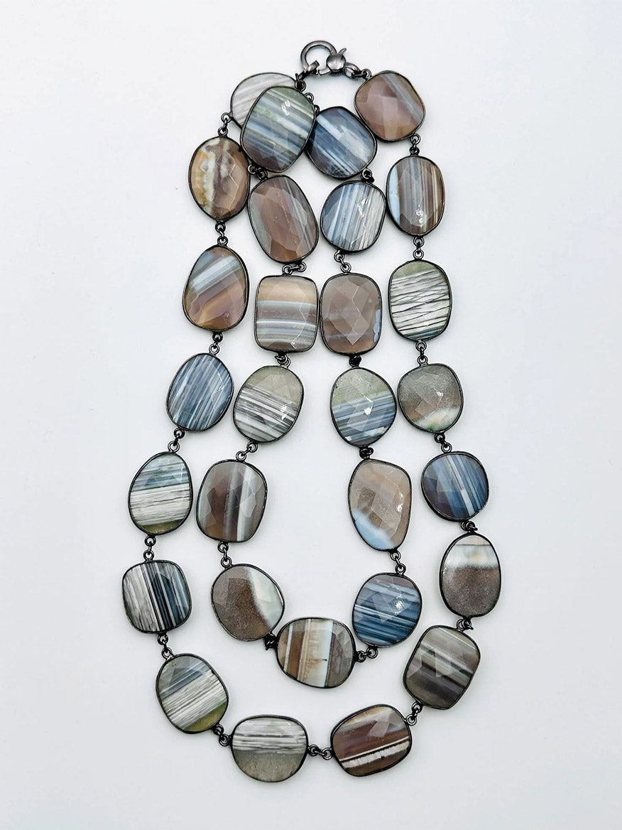 The JMNYC Designs Large Blue Lace Agate Necklace With Rhodium Bezel & Clasp 36" features double layers of flat, irregular oval Blue Lace Agate stones with gray, brown, and white stripes linked by rhodium-plated metal.