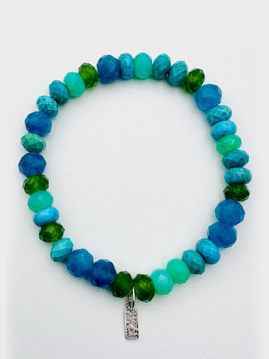 The JMNYC Designs Canadian Jade, Apatite, Chrysoprase, and Turquoise Stretch Bracelet features a petite diamond dog tag charm and faceted beads in green and blue hues, shown on a white background.