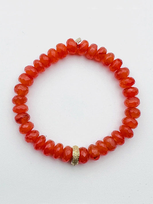 The JMNYC Designs AAA Faceted Carnelian 8-9mm Stretch Bracelet showcases translucent red beads and a central gold-toned accent, elegantly presented on a plain white background.