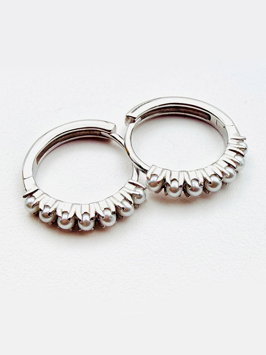 JMNYC Designs Freshwater Pearl Earrings on Sterling Silver Huggie are displayed on a white background, featuring a pair of sterling silver huggie earrings each accented with a row of small freshwater pearls along the lower edge.