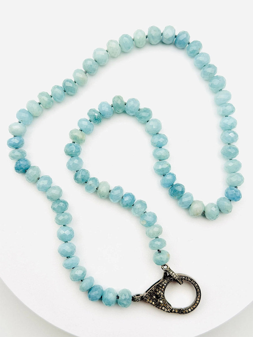 The JMNYC Designs Faceted Aquamarine Rondelle Necklace with Sterling Silver Diamond Clasp, featuring light blue faceted rondelle beads and a decorative sterling silver clasp, is displayed on a white surface.