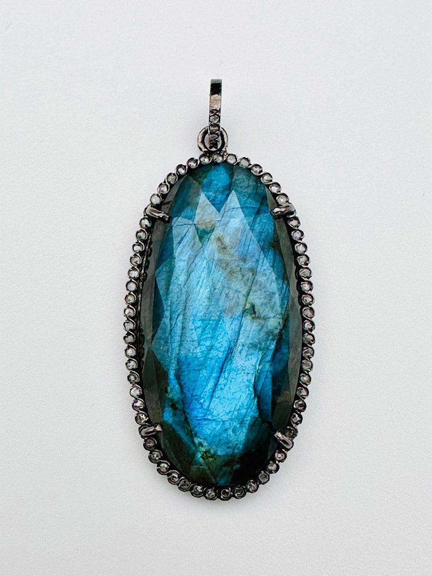 JMNYC Designs Faceted Oval Labradorite with Sterling Silver & Diamond Pendant, featuring an oval-shaped faceted labradorite stone set in dark sterling silver and accented with a border of small clear diamonds, displayed against a white background.