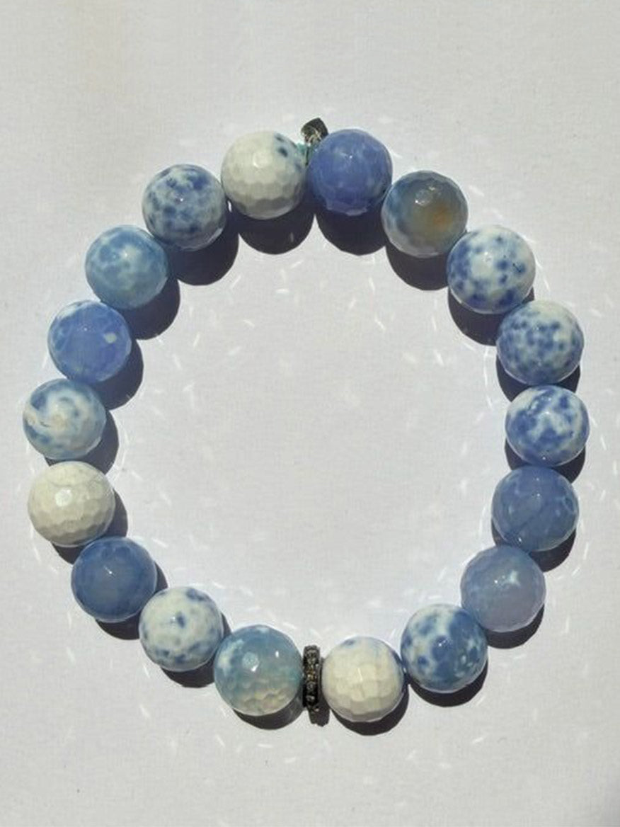 A JMNYC Designs Faceted Periwinkle Agate Ball Bracelet with Diamond Rondelle, 7.25", featuring round, blue and white marbled agate stones and a sparkling diamond-accented rondelle, arranged in a circle on a white background.