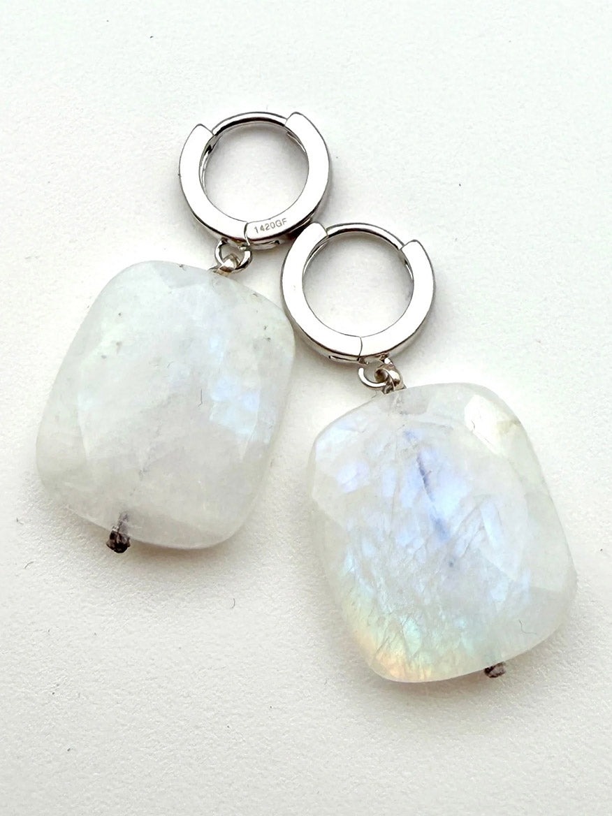 A pair of JMNYC Designs Flat Faceted Rainbow Moonstone Earrings, each featuring a rectangular rainbow moonstone pendant with subtle iridescent reflections, set on sterling silver huggie hoops—perfect for those seeking an elegant faceted earring with timeless charm.