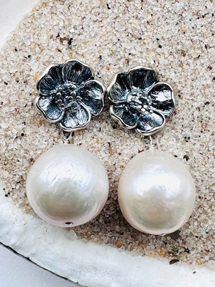 JMNYC Designs Medium White Baroque Pearl Earrings on Sterling Silver Peony Post, displayed on a sandy textured surface.