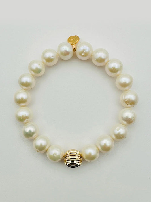 The JMNYC Designs 10mm Round Freshwater Pearl Bracelet features a single ridged gold filled ball and a small gold charm.