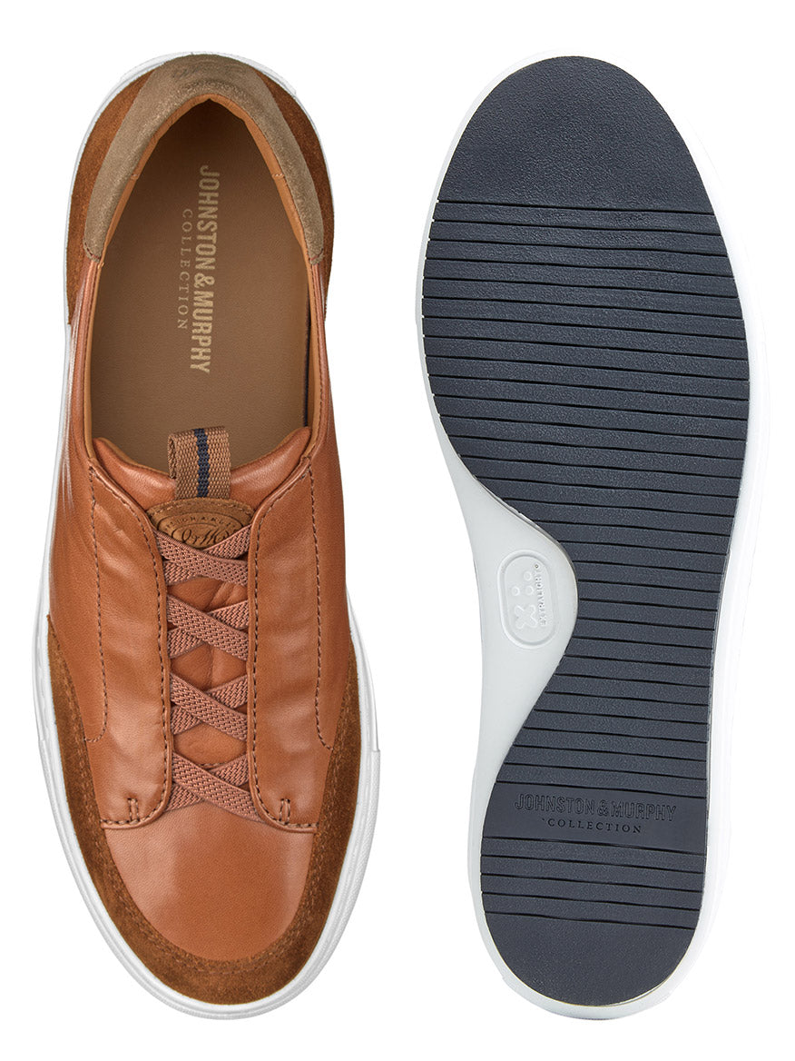 A pair of J & M Collection Anson Stretch Lace-to-Toe Cognac English Suede/Sheepskin sneakers with retro styling, cushioned EVA outsoles, and white soles. One shoe is shown from the top, and the other from the bottom. Both prominently display the "Johnston & Murphy Collection" brand.