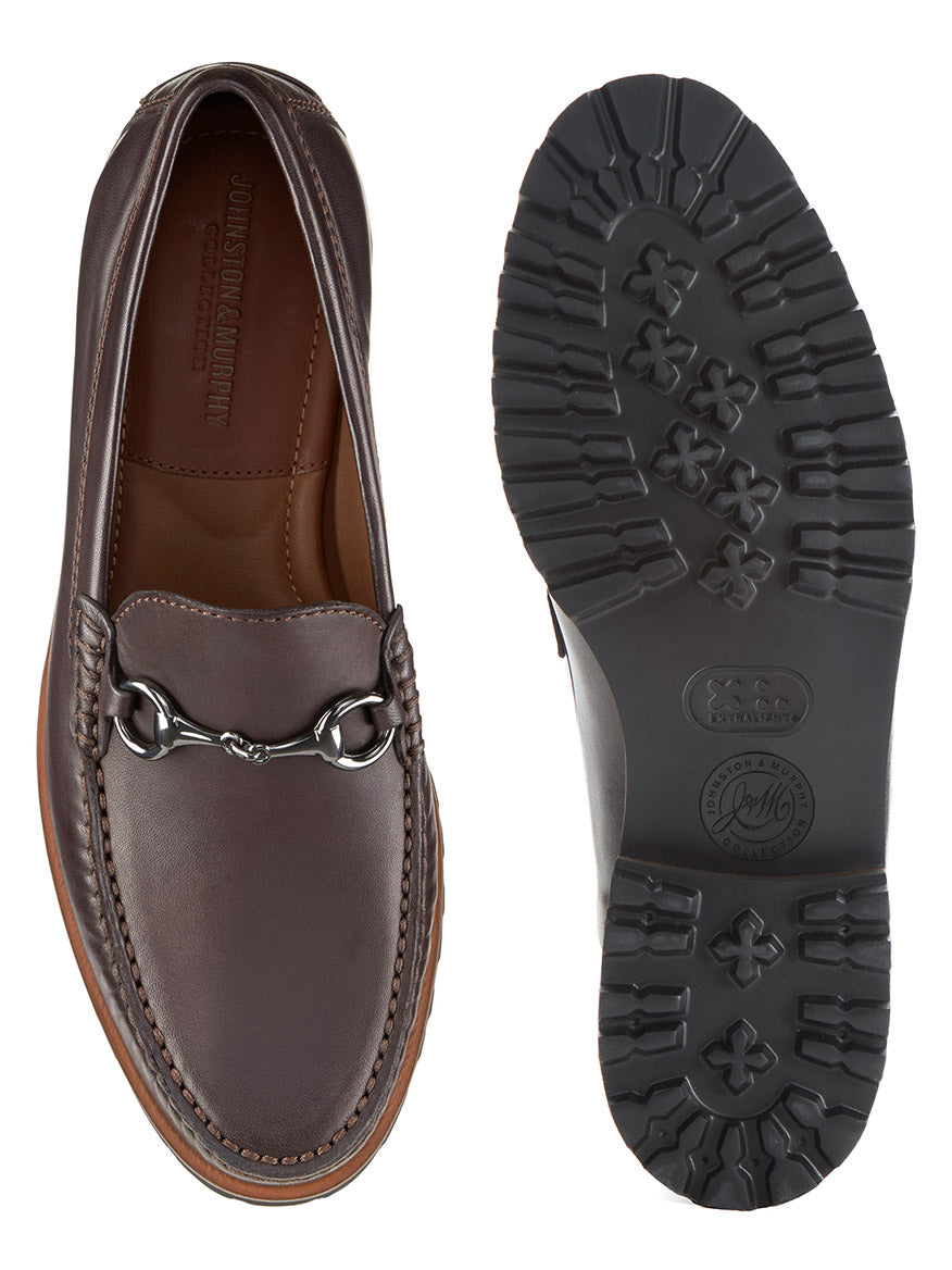 The J & M Collection Baldwin Lug Bit in Dark Brown Sheepskin is shown from above and below, featuring a metal horsebit detail, leather-lined interior, and a textured rubber sole with floral-patterned treads.