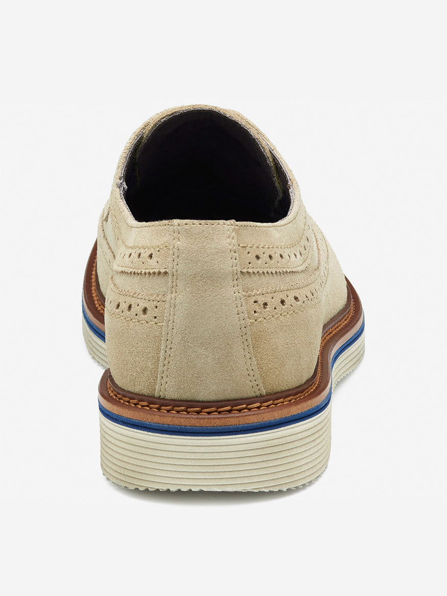 The J & M Collection Jenson Longwing in Taupe Italian Suede showcases a rear view of beige suede with decorative perforations and a layered EVA sole featuring a blue stripe, brown trim, and a leather-covered footbed for added comfort.