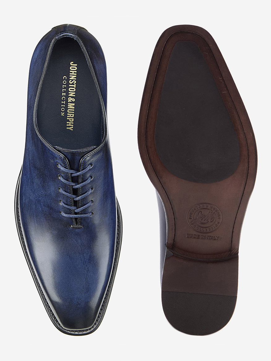 A pair of J & M Collection Larson Plain Toe shoes, shown from the top and sole, crafted in navy Italian calfskin. The top shoe displays "Johnston & Murphy Collection" branding, while the brown leather sole shows a logo with "Made in Italy.