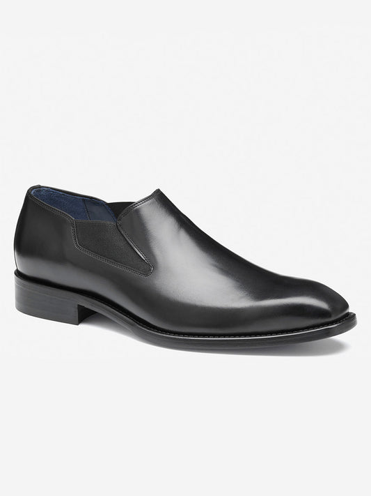 The J & M Collection Larson Slip-On in Black Italian Calfskin is a sleek dress shoe with a black leather design, featuring a low heel and elastic side panels.