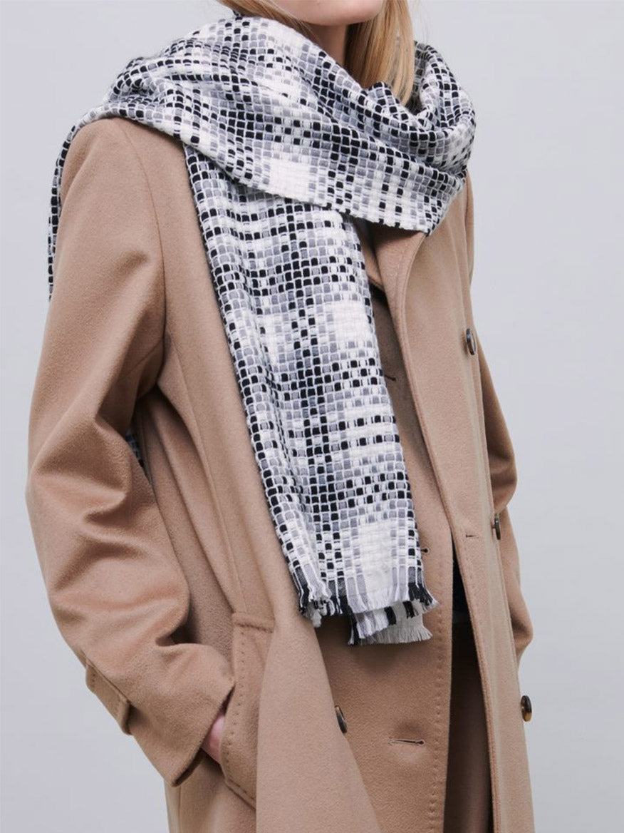 Woman in a beige coat wearing a Jane Carr The Plaid Scarf in Black/White with frayed hems.