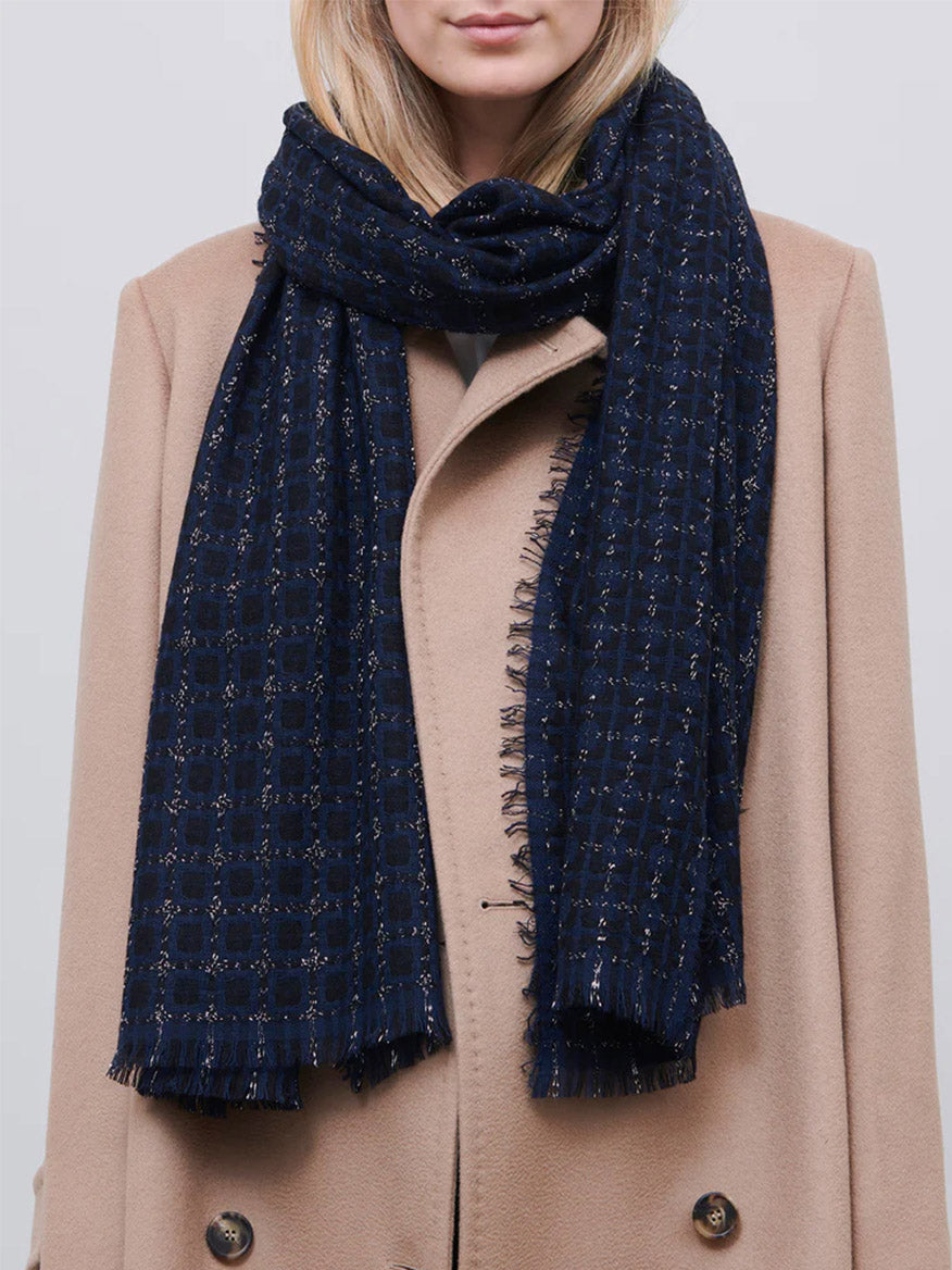 A person wearing a beige cashmere coat and a Jane Carr The Tile Scarf in Black/Navy.