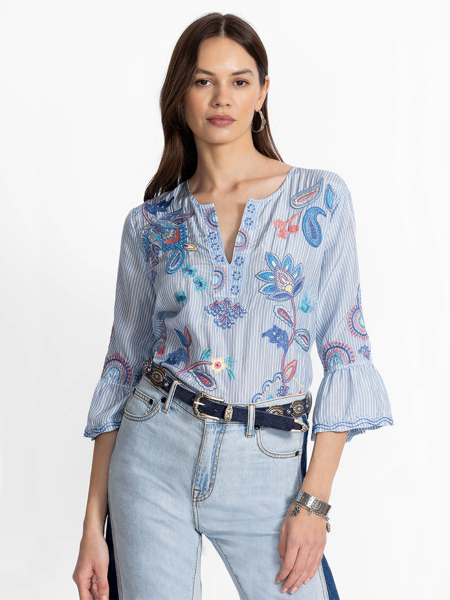 A woman in a luxurious Johnny Was Ruffle Sleeve Blouse in Barine Stripe Bar with light jeans stands against a plain background.