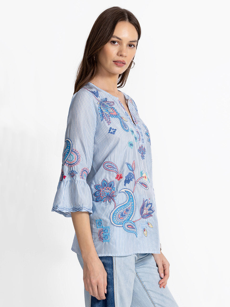 A woman in a Johnny Was Ruffle Sleeve Blouse in Barine Stripe Bar poses sideways against a plain background, her jeans adding the perfect casual touch.