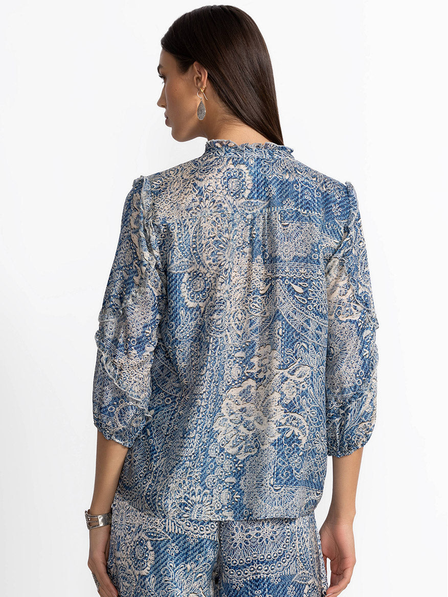 A woman stands with her back to us, wearing the Johnny Was Zeeland Blouse in Denim Print. The intricate detailing adds elegance, while the denim-inspired print gives it a modern flair.