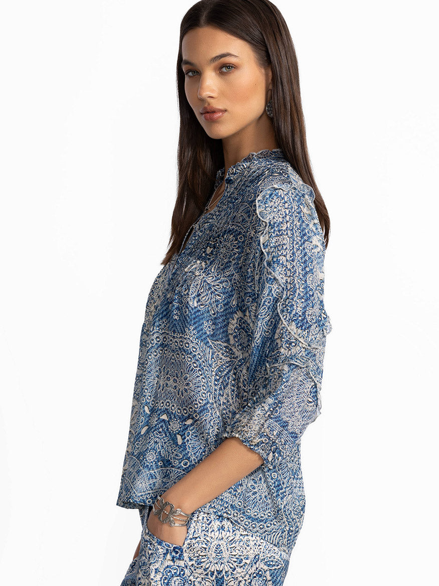 A woman in the Johnny Was Zeeland Blouse in Denim Print and matching pants stands sideways against a plain background, highlighting the intricate detailing of her ensemble.