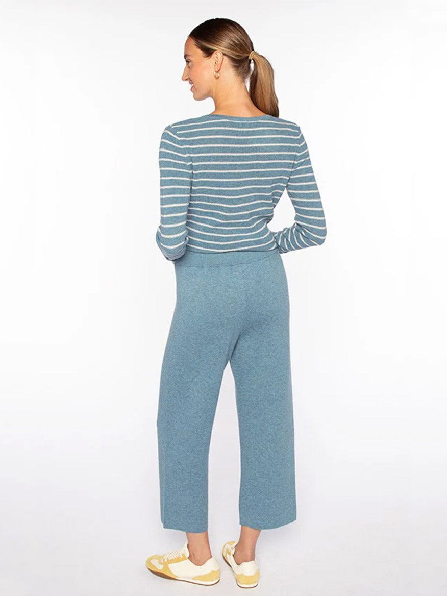 A woman stands facing away, wearing a blue and white striped long-sleeve top, Kinross Doubleknit Crop Pant in Denim with a cropped length, and yellow sneakers against a plain white background.