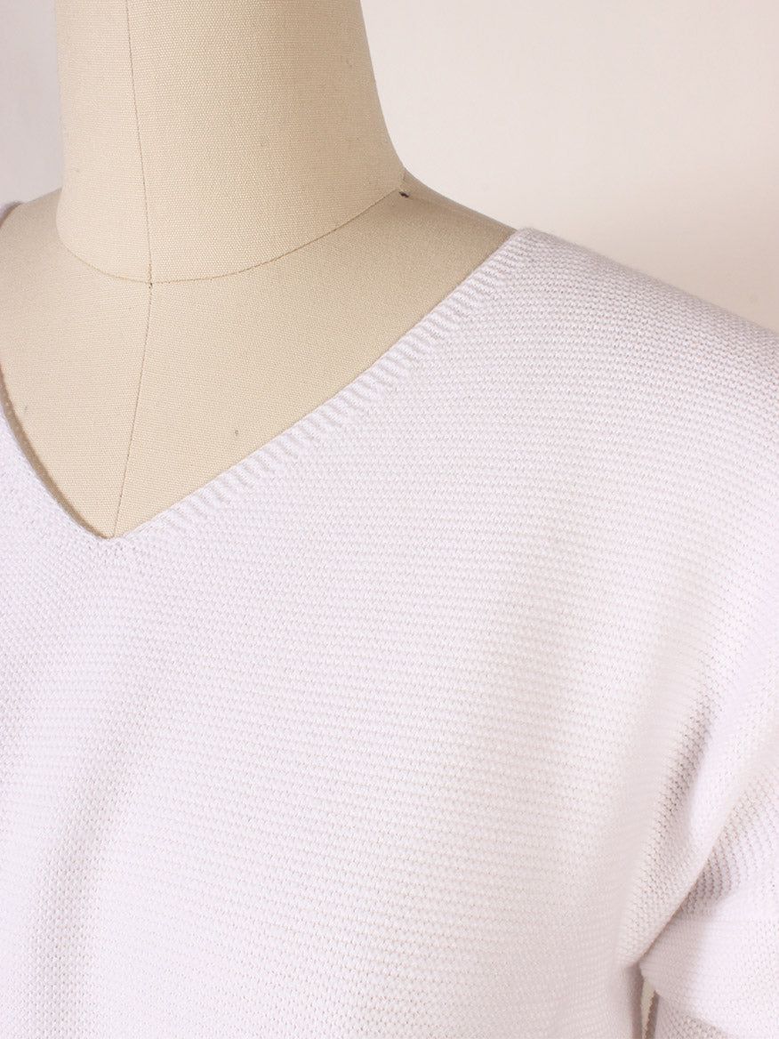A close-up of a mannequin wearing the Kinross Garter Easy Vee in White, showcasing its textured fabric, V-neckline, and ribbed cuffs.