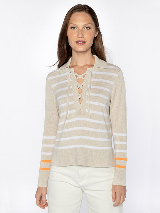 A person with long brown hair is wearing a beige and white striped polo with an orange accent and white pants. The Kinross Stripe Lace Up Polo in Champagne/White/Papaya features a lace-up front.