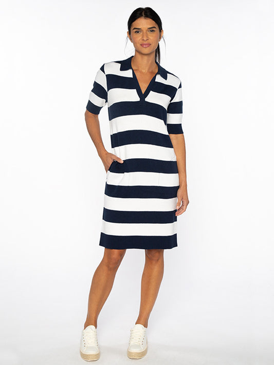 A person in a Kinross Splitneck Stripe Polo Dress in Navy/White with knee length hem and white sneakers stands against a plain white background.