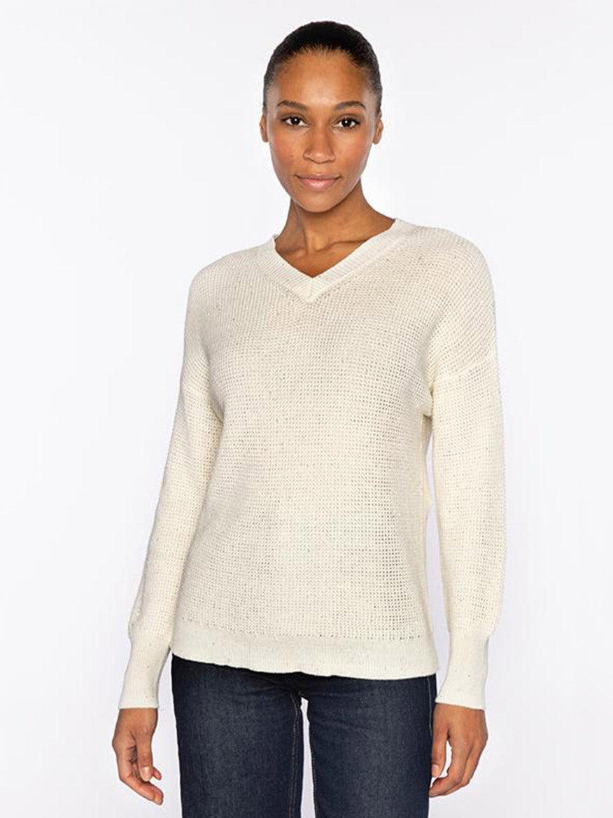 A woman faces forward wearing the Kinross Thermal Sequin Vee in Cream, a premium cotton knit sweater with long sleeves, paired with dark jeans, set against a plain white background.