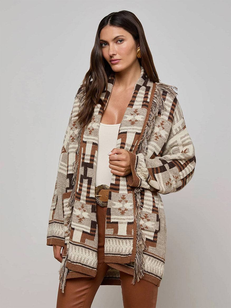 A woman wears the L'Agence Jair Cardigan in Natural Multi over a beige top and brown pants, standing against a plain light background.