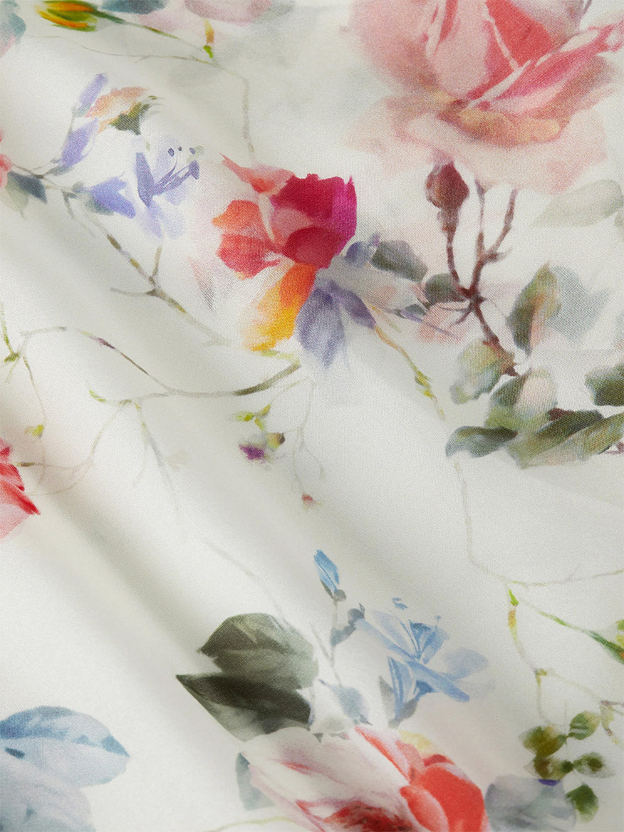 A close-up of L'Agence Miki Silk Dress in Ivory Multi Watercolor Dusty Floral, showcasing white silk chiffon with a watercolor floral print of roses and green leaves in red, pink, purple, and blue—ideal for an elegant look.