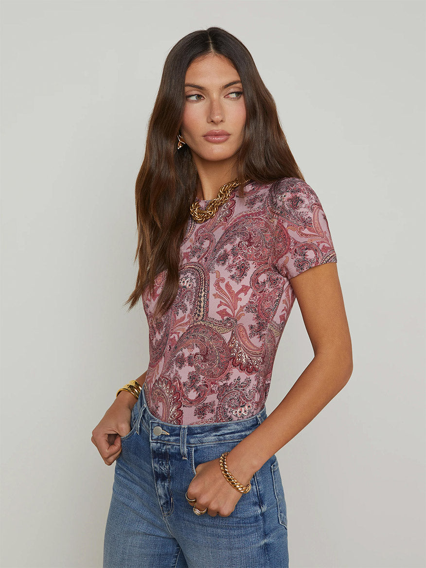 Woman wearing the L'Agence Ressi Fitted Tee in Mauve Multi French Paisley, paired with blue jeans and gold jewelry, standing against a plain background.