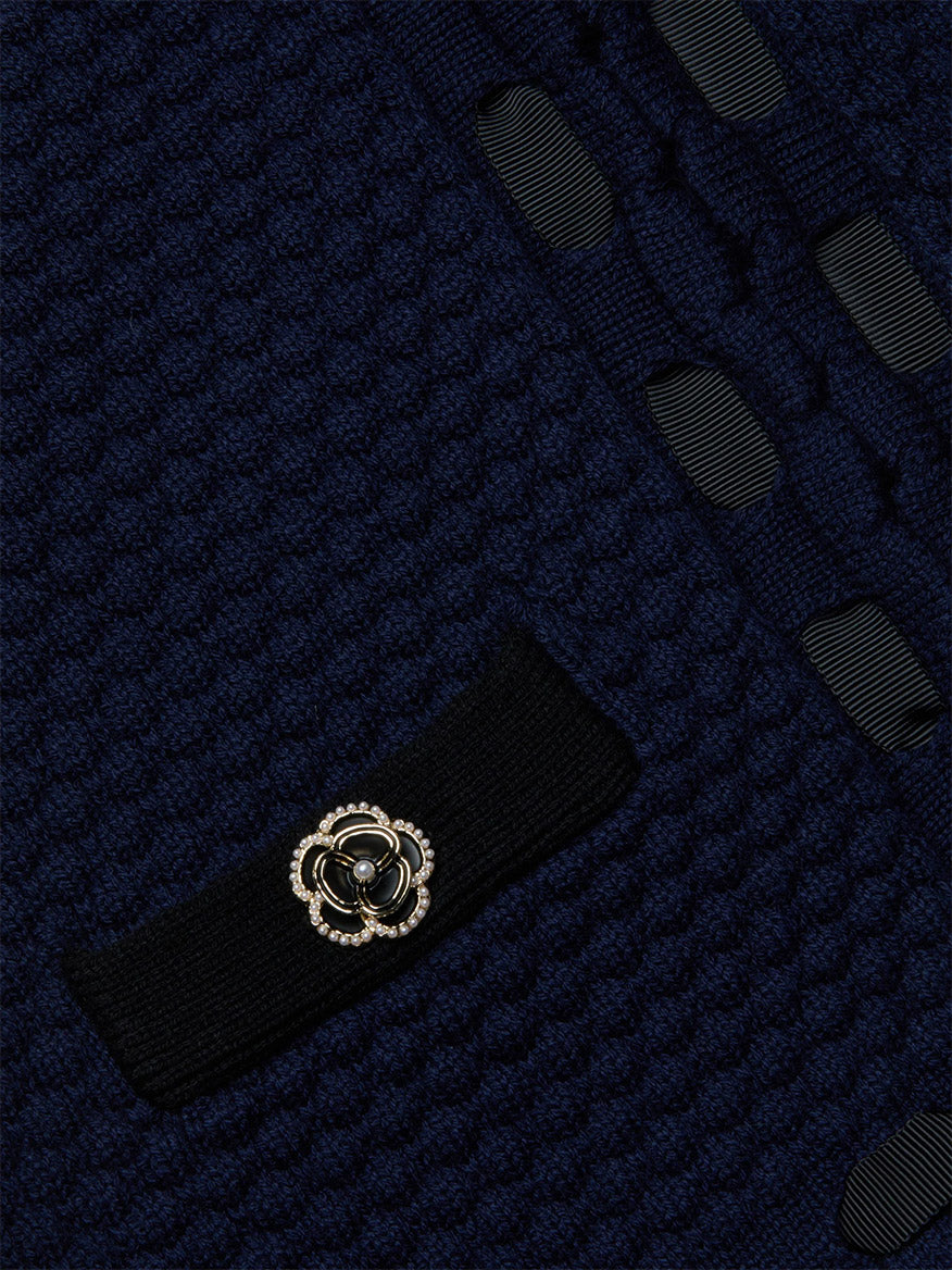 Close-up of the L'Agence Astor Cardigan in Midnight/Black, showing textured knit midnight blue fabric, black trim, a gold and black decorative button, and woven ribbon details.