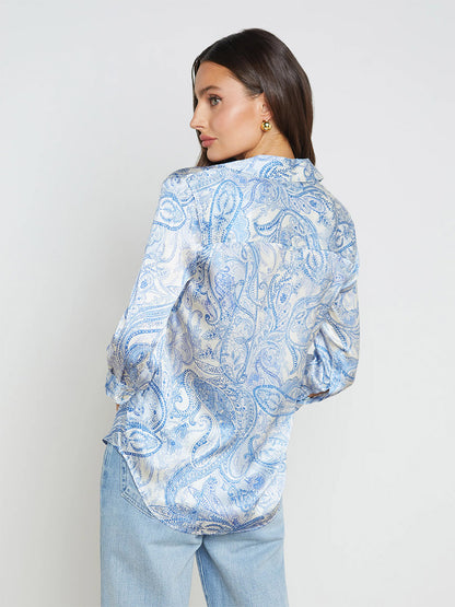 Woman wearing a L'Agence Dani Blouse in Ivory/Blue Decorated Paisley and jeans, standing with her back to the camera, looking over her shoulder.