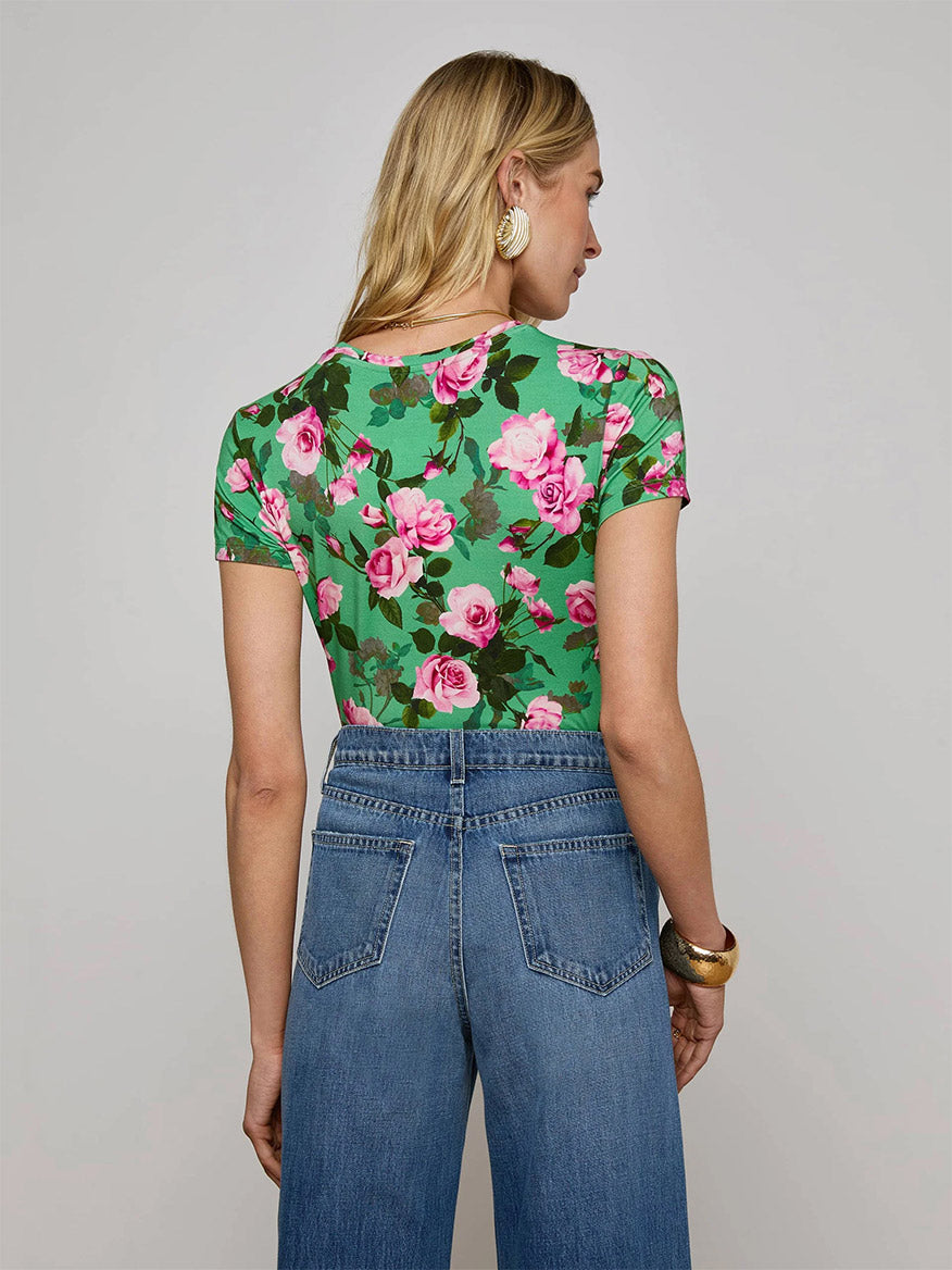 A woman with blonde hair is shown from the back, wearing the L'Agence Ressi Fitted Tee in Green Multi Santa Fe Rose and high-waisted blue jeans.