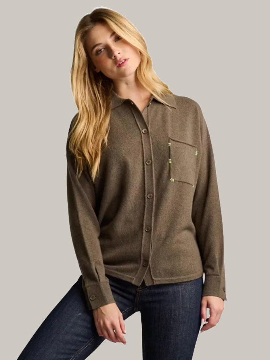 A woman wearing the Lisa Todd Big Shirt in Shale—a relaxed, earthtone button-down shirt with a chest pocket—paired with dark blue jeans and standing against a light gray background.