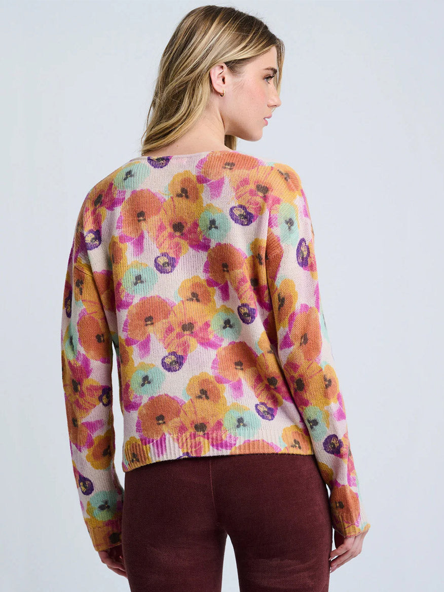 Woman facing away, wearing the Lisa Todd Bloomin' Cardigan in Frost Combo with a colorful floral print and maroon pants, against a light background.