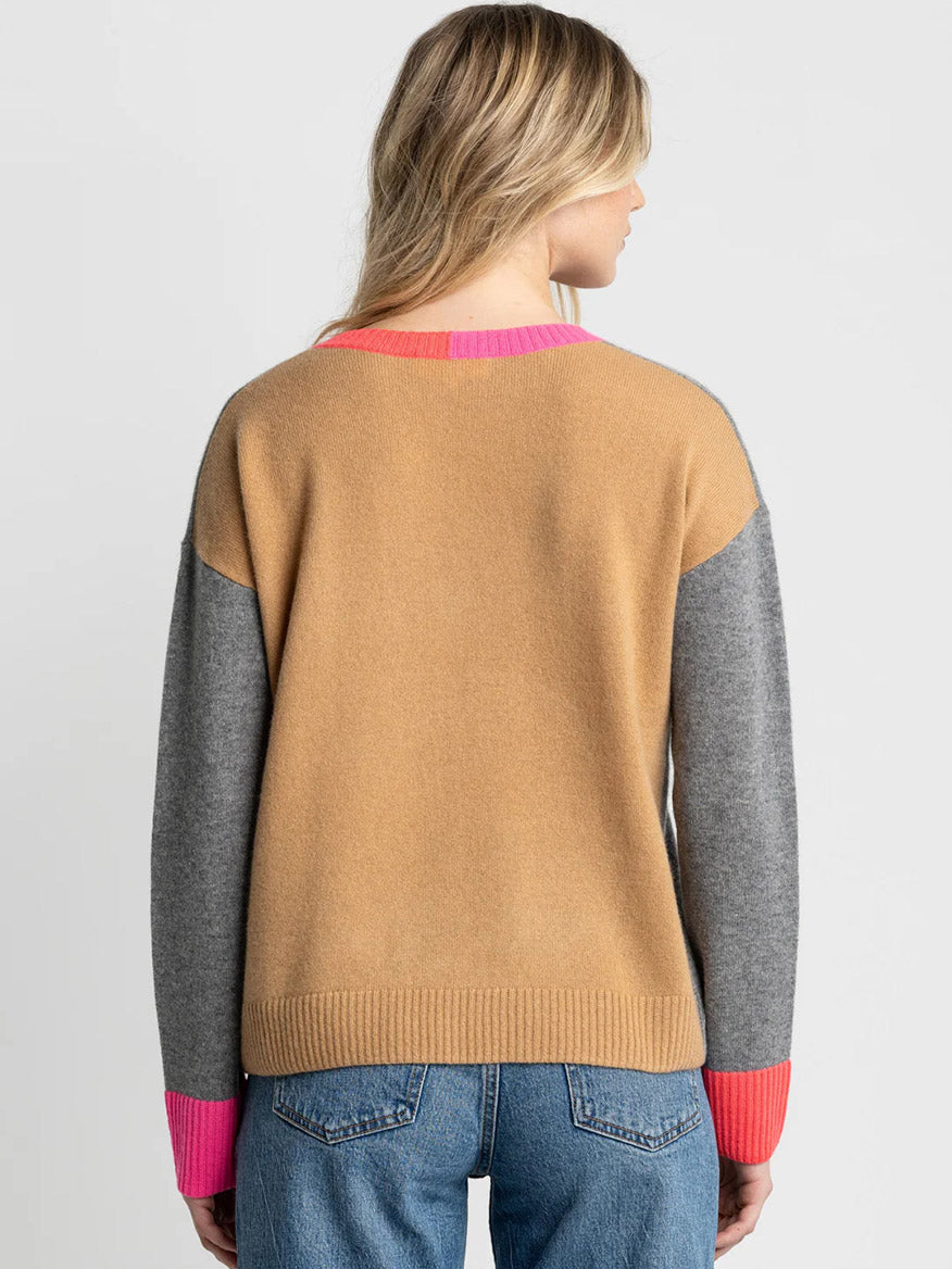 A person with long blonde hair, facing away from the camera, wears the Lisa Todd Color Wheel Sweater in Fog/Caramel—featuring a relaxed fit and colorblock design—paired with blue jeans.