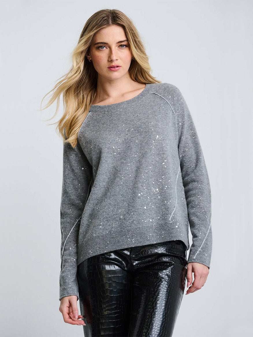 A woman wears the Lisa Todd Diamond Dust Sweater in Fog—a gray relaxed fit—paired with black textured pants, standing against a plain light background.