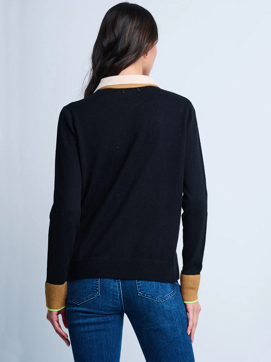 A person stands facing away, wearing the Lisa Todd Double Down Sweater in Black with tan cuffs and collar, styled in a true fit silhouette, paired with blue jeans.