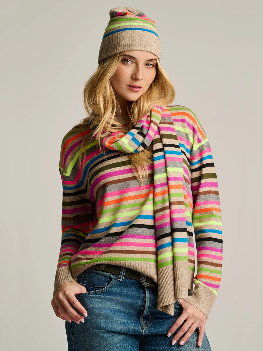 Woman in a relaxed fit striped sweater, blue jeans, and the Lisa Todd Hype The Stripe Hat in Oat Multi Stripe, standing against a plain background.