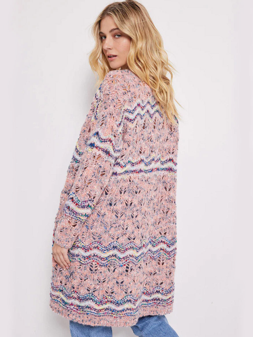 A woman in a Lisa Todd Lofty Lover Cardigan in Pink Multi looking over her shoulder.
