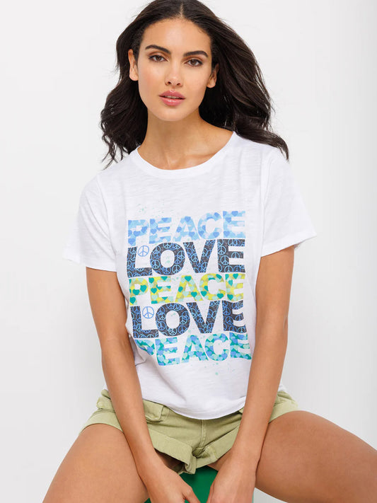 A woman in a Lisa Todd Peace Please Crew in White with the words "Peace and Love" printed in colorful graphic design, sitting with crossed arms.