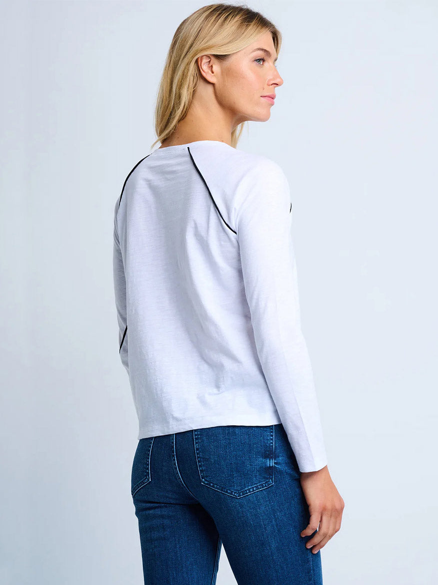 A woman wears the Lisa Todd Piping Hot Tee in White—a cotton slub long-sleeve crew with black piping—paired with blue jeans, shown from the side and back against a plain light background.