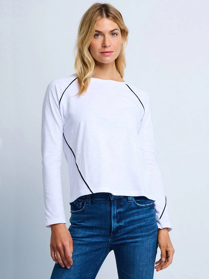 A woman wears the Lisa Todd Piping Hot Tee in White with black piping details and blue jeans, standing against a plain light background.