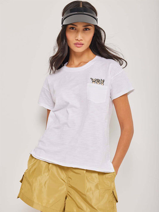 Woman in a Lisa Todd Pocket Pups Tee in White and yellow shorts, paired with a black visor, standing against a neutral background.
